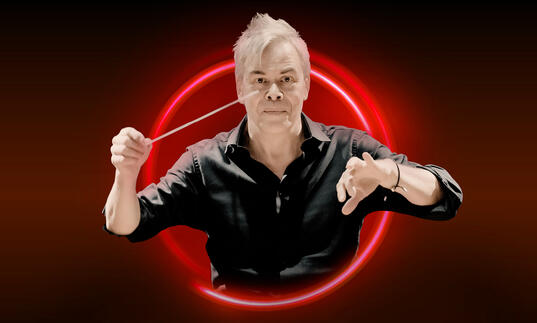 Hannu Lintu with his arms raised against a red bakcground