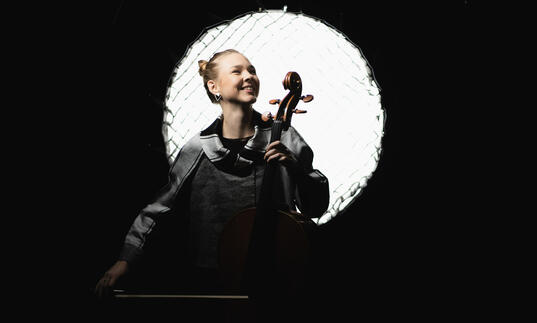 Valerie Fritz holding a cello in front of a stage light