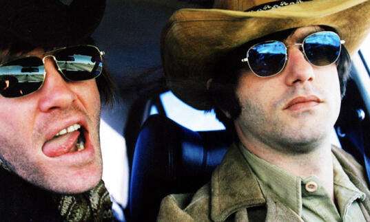 Two men sit in a vehicle wearing sunglasses. 
