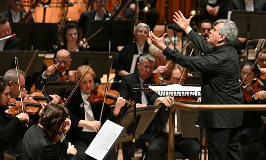 Sir Antonio Pappano conducting the London Symphony Orchestra, facing the Orchestra on the conductor's podium, with both hands raised in the air