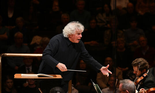 Sir Simon Rattle conducting from the podium in the Barbican concert hall