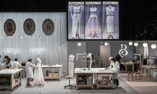 Image of a set with tables and mirrors where people are working together to create a dress