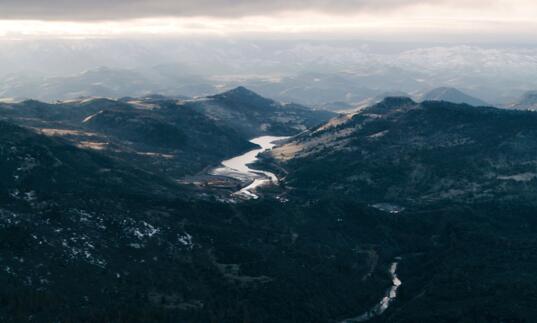 A mountainous landscape, with a reservoir and dam in the foreground and a river winding through the hills beyond.