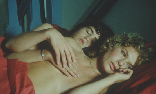 A still from A Woman Like Eve, showing two naked women embracing in bed.