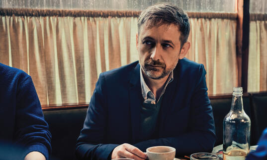 Neil Hannon sitting at a table drinking coffee