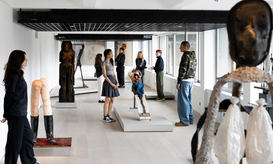 A group of people stand in an exhibition of sculpture in a sunny room.