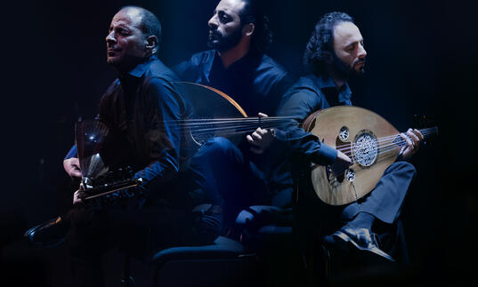 trio playing string instrument and singing in dramatic lighting
