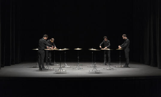  4 percussionists standing around an installation of 12 suspended cymbals