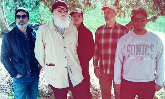 the five band members are standing under a tree on a sunny day