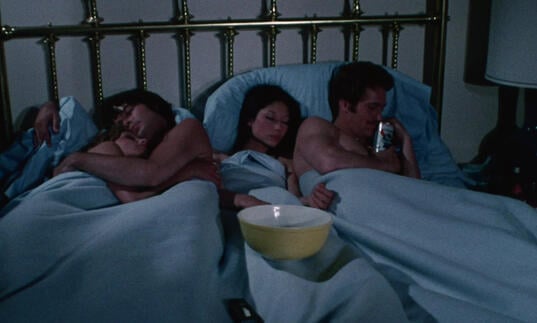 Two couples lie in bed together.