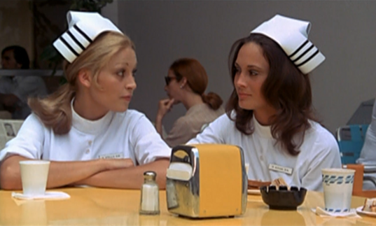 Two young student nurses sit at a lunch table.