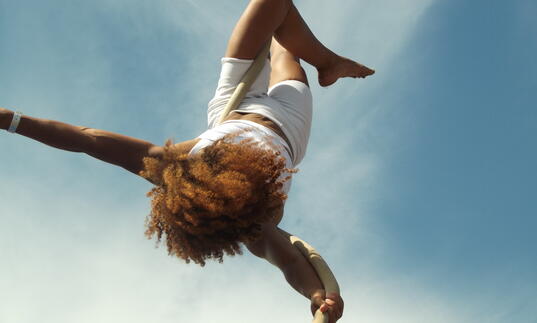 A person performing an aerial act hanging upside down from a rope