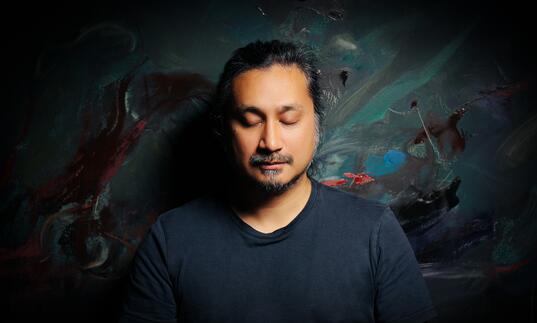 Headshot of an Asian man against a dim colourful background