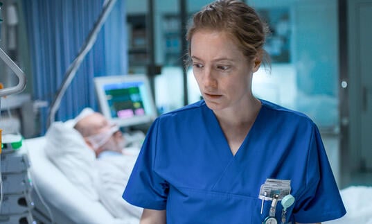 A nurse looks stressed, standing in a hospital