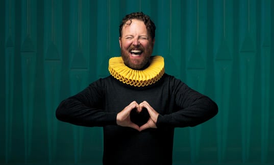 A person with a yellow collar around their neck makes a love heart symbol with their hands.