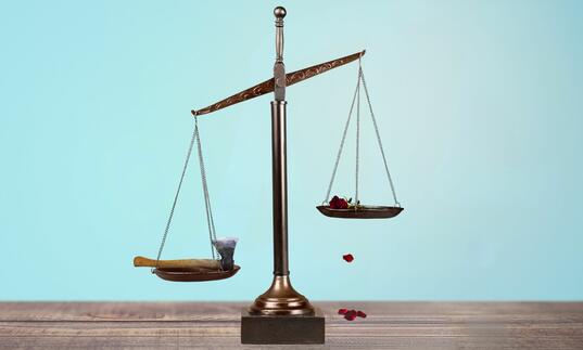 Scales of Justice, one side with an axe and one side with a red rose dropping petals on table