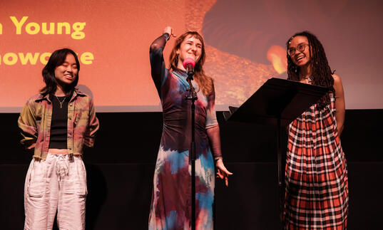 Three women stand on a stage performing