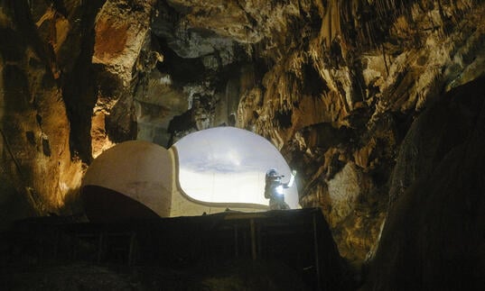a person in a spacesuit in a cave near a spaceship