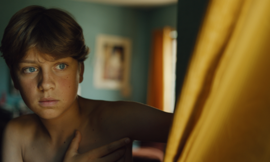 A young boy behind a curtain.