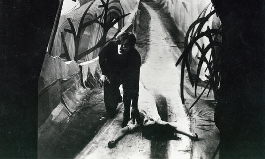 A man in a distorted walkway with a woman lying on the floor.