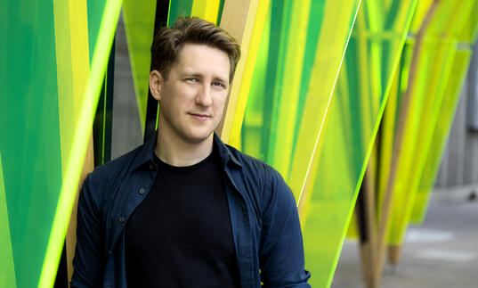 Conductor Joshua Weilerstein standing in front of vibrant green background