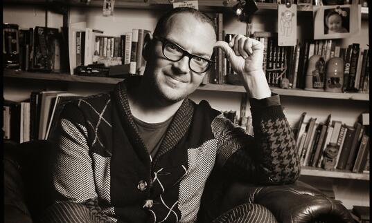 Black and white portrait of Cory Doctorow sitting in an armchair