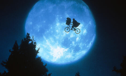 A bike floating in the sky with the moon as backdrop.