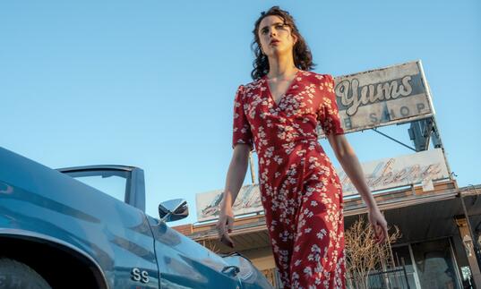 Margaret Qualley strides determinedly in a red floral dress