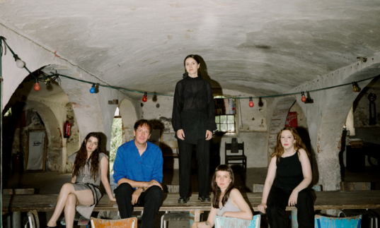 An image of Christian Loffler and band mates sat at a table in a rustic looking room