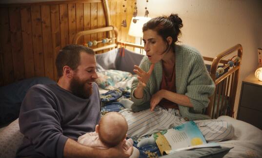 A young family sit in bed together, the mother signs 