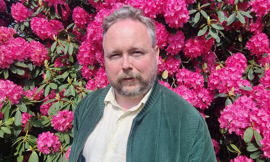 Richard Dawson stood in front of a wall of flowers
