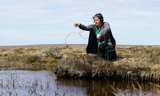 A person sat by a river bank with headphones on 