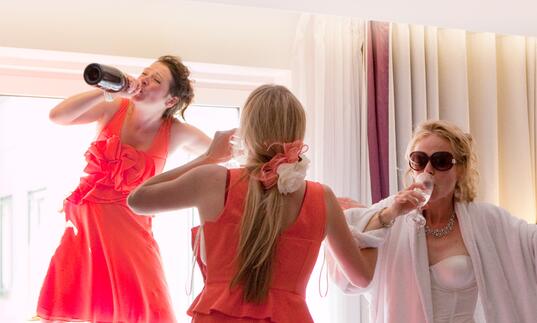 A bride and her two bridesmaids down prosecco in a hotel room.