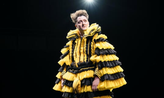 A person stood on stage wearing yellow and black 