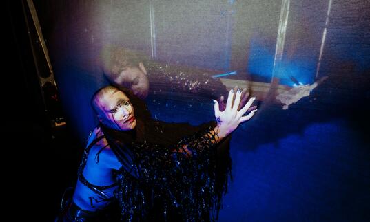 A person with a black veil over their arms presseing against a thin partiton while another person does the same on the other side