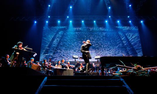 Tan Dun conducting an orchestra while the film plays behind them